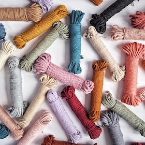 May include: A variety of colorful cotton rope cords in different colors, including red, blue, green, pink, and brown. The cords are arranged in a random pattern on a white surface.