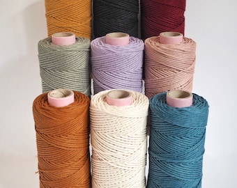 May include: Eight spools of cotton rope in various colors, including mustard yellow, gray, lavender, blush pink, natural white, rust orange, teal blue, and black. The spools are arranged in a staggered pattern.