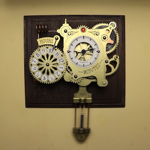 May include: A steampunk-style wall clock with brass gears and a pendulum. The clock face is white with black numerals and hands, and the words "HOURS" and "MINUTES" are visible. The clock is mounted on a dark wooden backing.