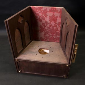 May include: A wooden box with a dark brown finish, featuring arched cutouts and a decorative red floral patterned interior. The box has a rectangular base with brass accents and a gold-colored metal piece on the side.
