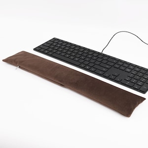 May include: A brown keyboard wrist rest with a zipper. The wrist rest is made of a soft, plush material. The wrist rest is lying on top of a black keyboard.
