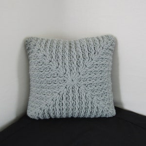 K&ouml;nnte beinhalten: Ein graues gestricktes Kissen mit einem strukturierten, gewebten Design. Das Kissen ist quadratisch und hat ein weiches, flauschiges Aussehen.