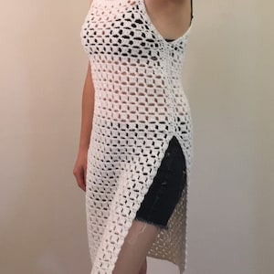 May include: White crochet top with a long, loose fit and side slits. The top has a square-shaped pattern and a scoop neck.