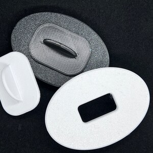 May include: Three oval-shaped plastic buttons with different sized holes in the center. The buttons are white and black.