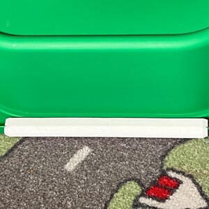 K&ouml;nnte beinhalten: Ein gr&uuml;ner Plastik-Aufbewahrungskasten mit einem wei&szlig;en Plastikrand am unteren Rand. Der Kasten steht auf einem gemusterten Teppich.