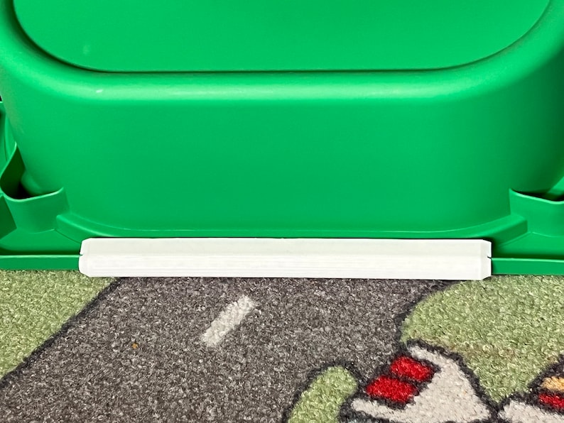 K&ouml;nnte beinhalten: Ein gr&uuml;ner Plastik-Aufbewahrungskasten mit einem wei&szlig;en Plastikrand am unteren Rand. Der Kasten steht auf einem gemusterten Teppich.
