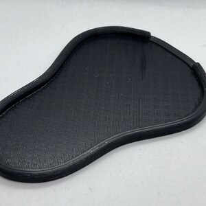 May include: A black, 3D printed, irregularly shaped tray with a raised edge.