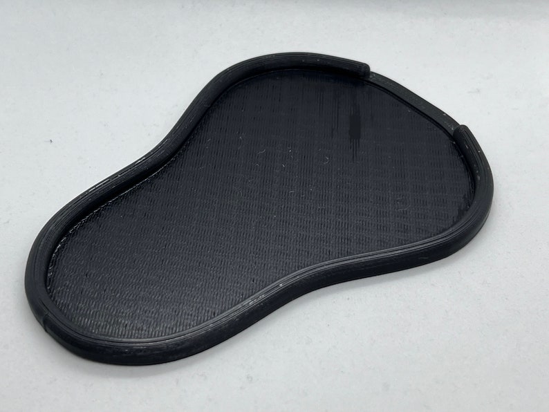May include: A black, 3D printed, irregularly shaped tray with a raised edge.