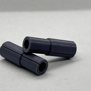 May include: Two gray plastic cylindrical objects with a groove running along the length of each object. The objects are stacked on top of each other.