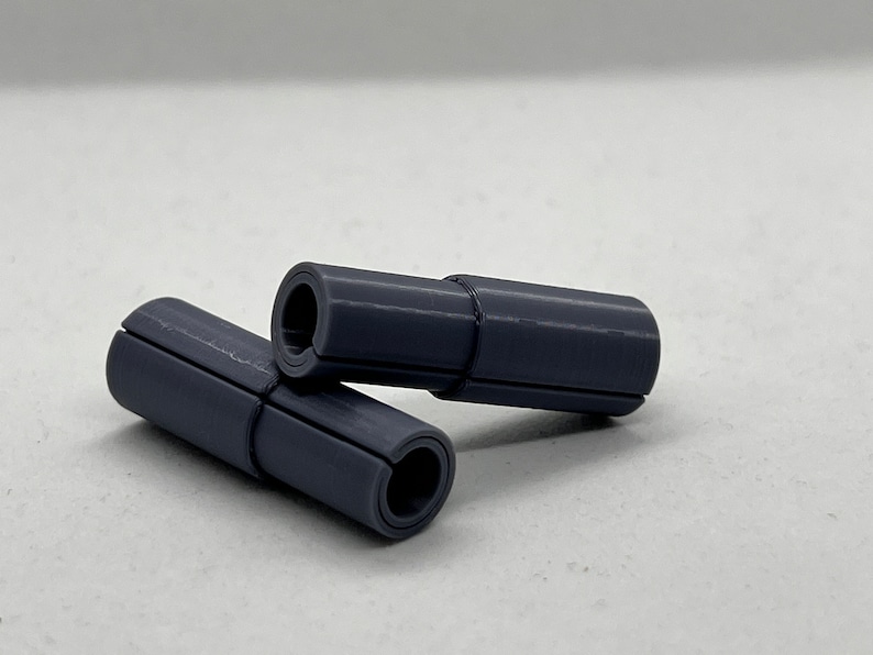 May include: Two gray plastic cylindrical objects with a groove running along the length of each object. The objects are stacked on top of each other.