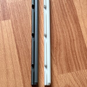 K&ouml;nnte beinhalten: Zwei Plastikst&uuml;cke, eines schwarz und eines wei&szlig;, mit einer Reihe von Schlitzen &uuml;ber die gesamte L&auml;nge. Beide sind etwa 12,5 cm lang.