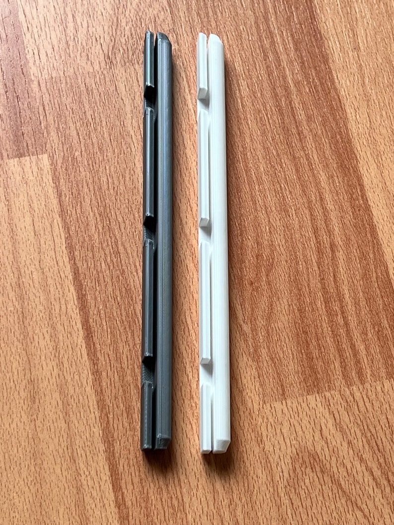 K&ouml;nnte beinhalten: Zwei Plastikst&uuml;cke, eines schwarz und eines wei&szlig;, mit einer Reihe von Schlitzen &uuml;ber die gesamte L&auml;nge. Beide sind etwa 12,5 cm lang.