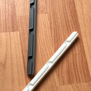 K&ouml;nnte beinhalten: Zwei 3D-gedruckte Kunststoffteile, eines schwarz und eines wei&szlig;, mit einer Reihe von rechteckigen Ausschnitten entlang der L&auml;nge jedes Teils.