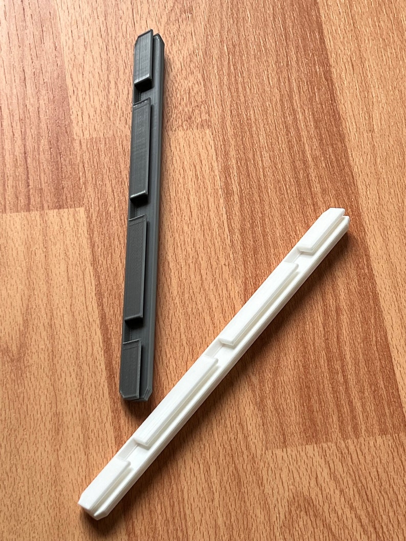 K&ouml;nnte beinhalten: Zwei 3D-gedruckte Kunststoffteile, eines schwarz und eines wei&szlig;, mit einer Reihe von rechteckigen Ausschnitten entlang der L&auml;nge jedes Teils.