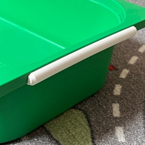 K&ouml;nnte beinhalten: Gr&uuml;ne Plastik-Aufbewahrungsbox mit wei&szlig;em Griff. Die Box hat eine glatte Oberfl&auml;che und ist aus strapazierf&auml;higem Kunststoff.