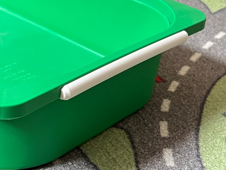 K&ouml;nnte beinhalten: Gr&uuml;ne Plastik-Aufbewahrungsbox mit wei&szlig;em Griff. Die Box hat eine glatte Oberfl&auml;che und ist aus strapazierf&auml;higem Kunststoff.