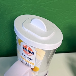 May include: White plastic pump bottle of Sagrotan Hygiene Seife Hydra Care hand soap with a white lid and a daisy design on the label. The label says "No Touch Nachf&uuml;ller 92% nat&uuml;rlichen Ursprungs".
