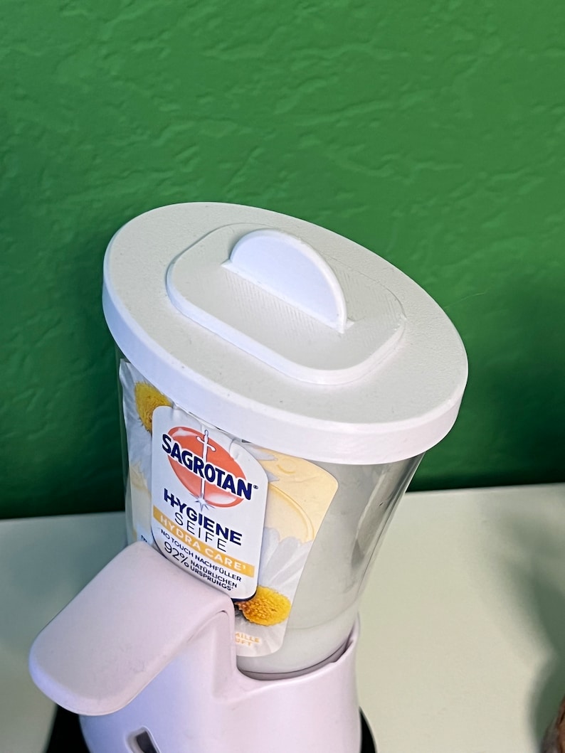 May include: White plastic pump bottle of Sagrotan Hygiene Seife Hydra Care hand soap with a white lid and a daisy design on the label. The label says "No Touch Nachf&uuml;ller 92% nat&uuml;rlichen Ursprungs".
