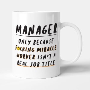 May include: White ceramic mug with the word "MANAGER" in black, above the text "ONLY BECAUSE F*CKING MIRACLE WORKER ISN'T A REAL JOB TITLE" in black and orange. A yellow smiley face replaces the "O" in "F*CKING".