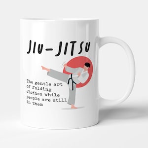 May include: White ceramic mug featuring a black and white illustration of a person performing a martial arts move. The text "JIU-JITSU" is at the top of the mug. The text below the illustration reads "The gentle art of folding clothes while people are still in them."