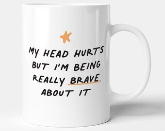 May include: White ceramic mug with a black star and the text "My head hurts but I'm being really brave about it" in black.