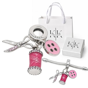 May include: A silver charm set featuring a pair of scissors, a spool of pink thread, and a pink button, all stamped with S925. The charms are displayed with a white gift bag and a small white box, both printed with the black text KABIKORNER.