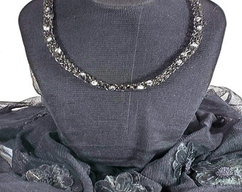 May include: A silver chain necklace with a delicate design, displayed on a black mannequin with a black sheer scarf with floral embellishments.