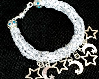 May include: A silver braided bracelet with blue rhinestone accents and multiple silver charms in the shape of stars and crescent moons.