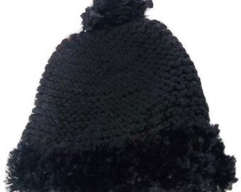 May include: A black knit hat with a fluffy pom-pom on top and a faux fur trim around the bottom. The hat is made of a thick, textured yarn, perfect for cold weather.