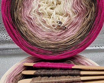 May include: A skein of ombre yarn in shades of pink, brown, and white. The yarn is wound into a ball and is ready to be used for knitting or crocheting.