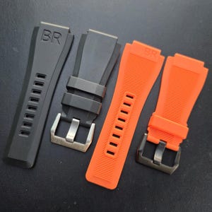 May include: Four watch straps are displayed. Two are black, and two are bright orange. Each strap features the letters "BR" embossed on the top. The black straps have silver buckles, and the orange straps have black buckles. All straps have rectangular holes.