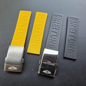 Könnte beinhalten: Nahaufnahme von Uhrenarmbändern und -schließen. Zwei gelbe und zwei schwarze Kautschukarmbänder werden mit silbernen Schließen gezeigt. Das Wort "BREITLING" ist auf die Armbänder geprägt. Die Schließen haben das Breitling-Logo und Text.