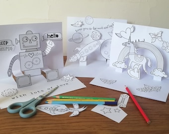 May include: Three pop-up cards with different designs: a robot, a rocket ship, and a unicorn. The cards are blank and ready to be colored. The text on the robot card says "BEEP BEEP!" and "hello". The text on the rocket ship card says "Love you to the moon and back". The text on the unicorn card says "with lots of love".