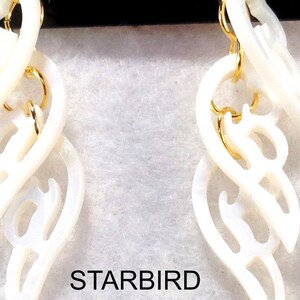 Puede incluir: Un par de pendientes de concha blanca con una cadena dorada y un dise&ntilde;o delicado e intrincado. Los pendientes tienen forma de una serie de corazones superpuestos.