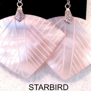 May include: A pair of fan-shaped earrings crafted from iridescent pale pink mother-of-pearl, featuring etched diagonal line patterns and silver-toned metal bails. The word STARBIRD is printed in black text at the bottom of the image.
