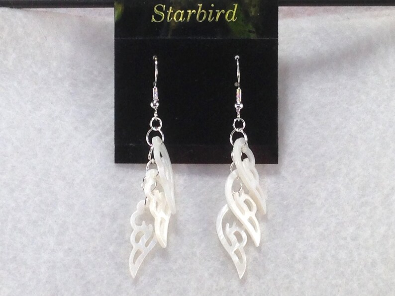 Puede incluir: Pendientes de concha blanca con un dise&ntilde;o delicado e intrincado. Los pendientes est&aacute;n hechos de m&uacute;ltiples capas de concha, cada una con una forma diferente. Los pendientes est&aacute;n suspendidos de ganchos de plata.