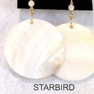 May include: A pair of white shell earrings with gold hooks. The earrings are round and have a smooth, pearlescent finish.