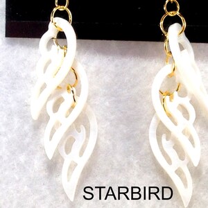 Puede incluir: Un par de pendientes blancos en forma de concha con detalles en metal dorado. Los pendientes est&aacute;n conectados por una cadena y tienen un dise&ntilde;o delicado e intrincado.