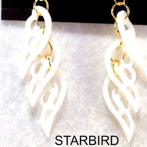 Puede incluir: Un par de pendientes blancos, tallados de forma intrincada, con detalles dorados. Los pendientes tienen forma de una serie de hojas superpuestas.