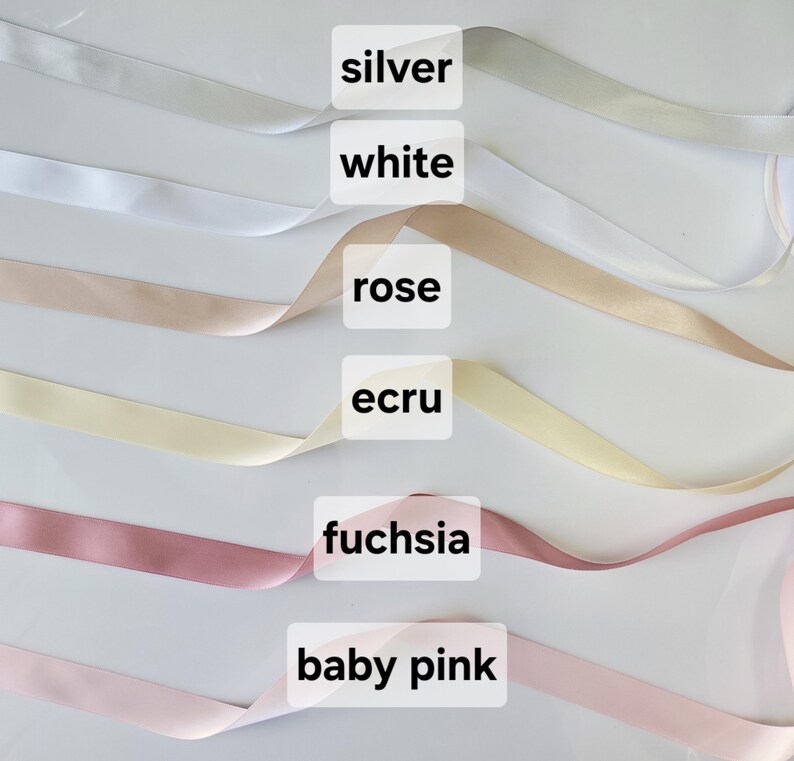 May include: A selection of satin ribbons in various colors, including silver, white, rose, ecru, fuchsia, and baby pink. Each ribbon is labeled with its corresponding color name in a white rectangular box. The ribbons are arranged diagonally across the frame.