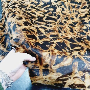 Op de afbeelding: Een close-up van een bruine en zwarte dierenprintstof met een zachte, pluche textuur.