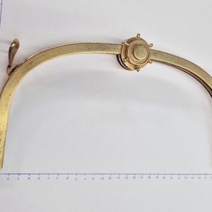 Può includere: Un telaio per borsa vintage in ottone con un design curvo. Il telaio presenta una chiusura circolare decorativa al centro e due bracci curvi con piccoli anelli su ciascuna estremità. Il telaio misura circa 15 cm di larghezza.