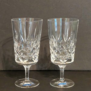May include: Two clear crystal glasses featuring a vertical starburst and diamond cut pattern on the bowl. Each glass has a smooth stem and a circular base, with a small blue Gorham brand sticker applied to the top of each base.