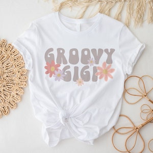 May include: White t-shirt with the text "Groovy Gig" in brown with pink and purple flowers.