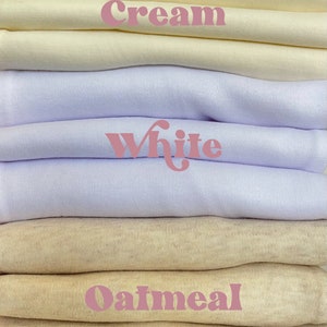 Puede incluir: Una pila de muestras de tela en color crema, blanco y avena. Los colores est&aacute;n etiquetados con las palabras "Crema", "Blanco" y "Avena".