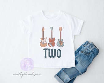 May include: White t-shirt featuring a graphic of three guitars and the word "TWO" in a bold font.