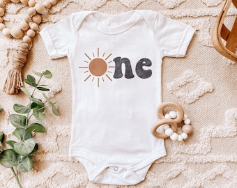 Peut inclure: Un body bébé blanc avec un soleil brun et du texte noir qui dit "one".