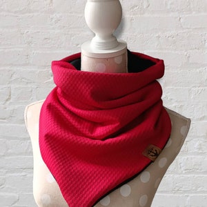 Könnte beinhalten: Ein roter und schwarzer Infinity-Schal mit einem strukturierten Muster. Der Schal ist gefaltet und auf einer Schaufensterpuppe ausgestellt.