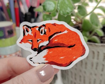 May include: A hand-drawn sticker of a curled up orange fox sleeping. The fox is drawn in a simple, cartoon style with a white background.