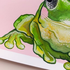 Peut inclure: Gros plan sur une grenouille verte avec un ventre rose et un &oelig;il noir. La grenouille est peinte dans un style aquarelle et a une apparence textur&eacute;e.